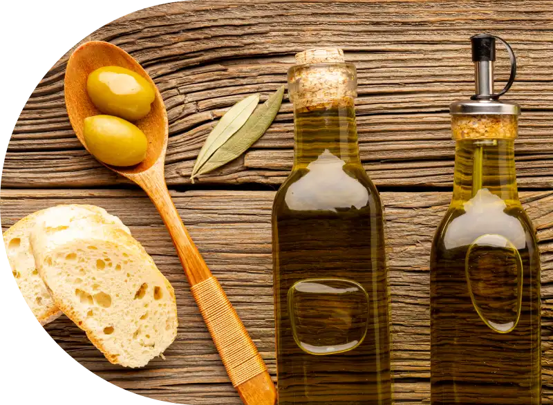Drie flessen olijfolie op een rustieke houten tafel, vergezeld van een houten lepel met twee groene olijven, sneetjes brood en een enkel olijfblad. Gezellig en natuurlijk.